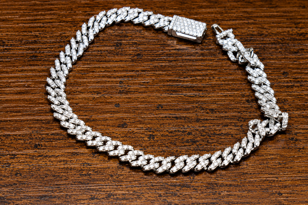 The VVS1 Moissanite Monaco Cuban Bracelet (5.8mm, 2.01 CTW, 925 Sterling Silver) with a jeweled rectangular clasp is displayed on a dark wooden surface, showcasing its sparkling elegance and luxurious design.