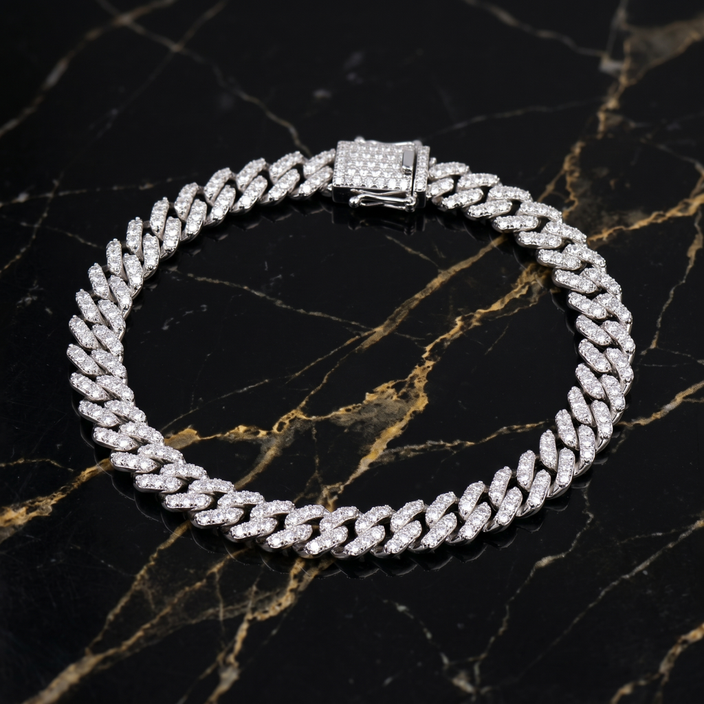 The VVS1 Moissanite Monaco Cuban Bracelet 5.8mm 2.01 CTW, crafted in 925 sterling silver, features a sparkling clasp and is elegantly displayed in a circular arrangement on polished black marble with white and gold veins.