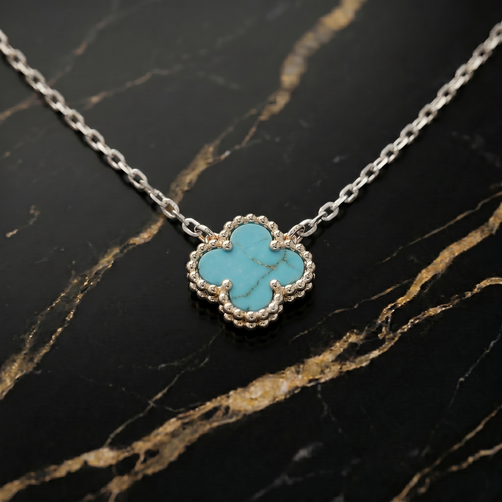 Turquoise clover-shaped pendant on a silver chain against a black marble background
