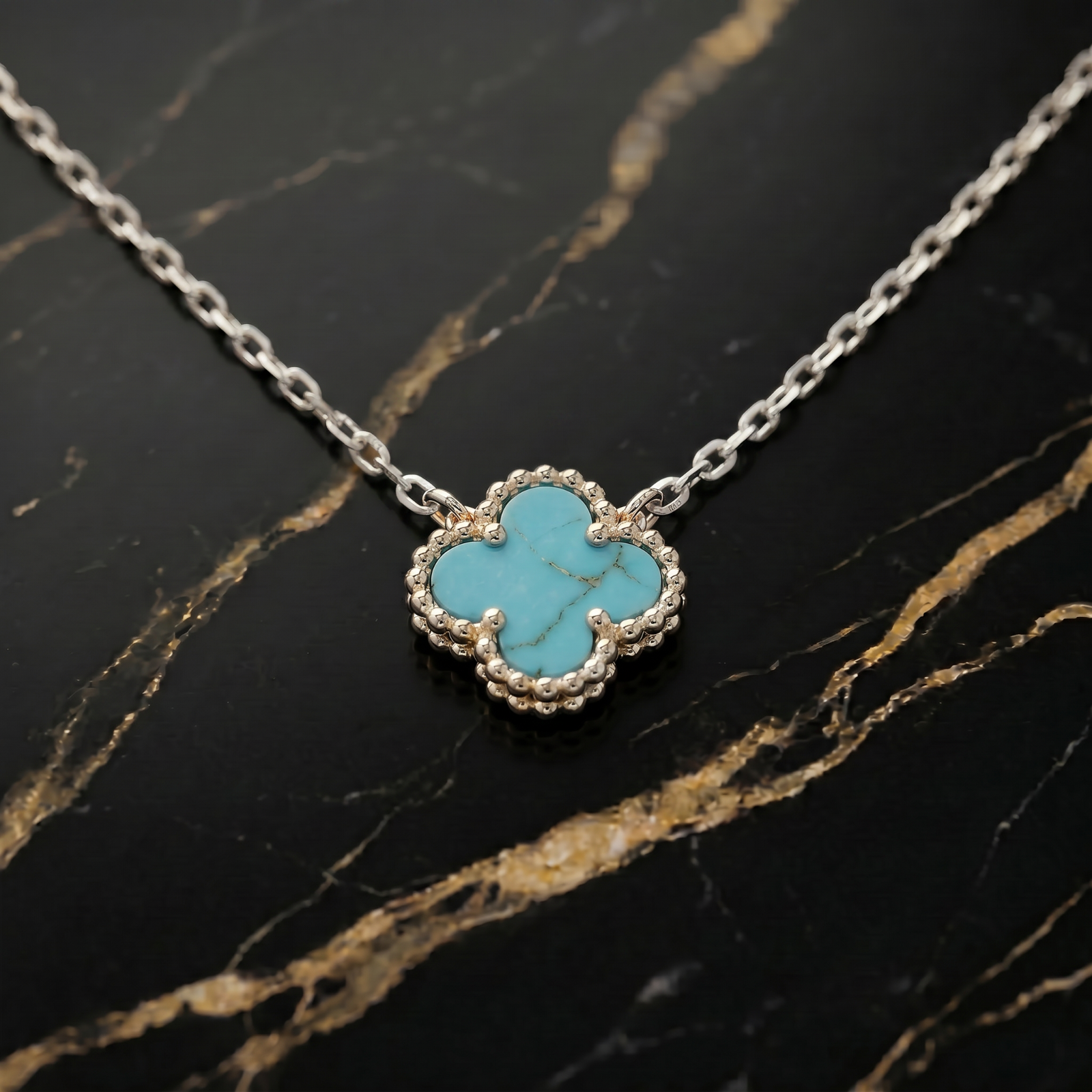 Turquoise clover-shaped pendant on a silver chain against a black marble background