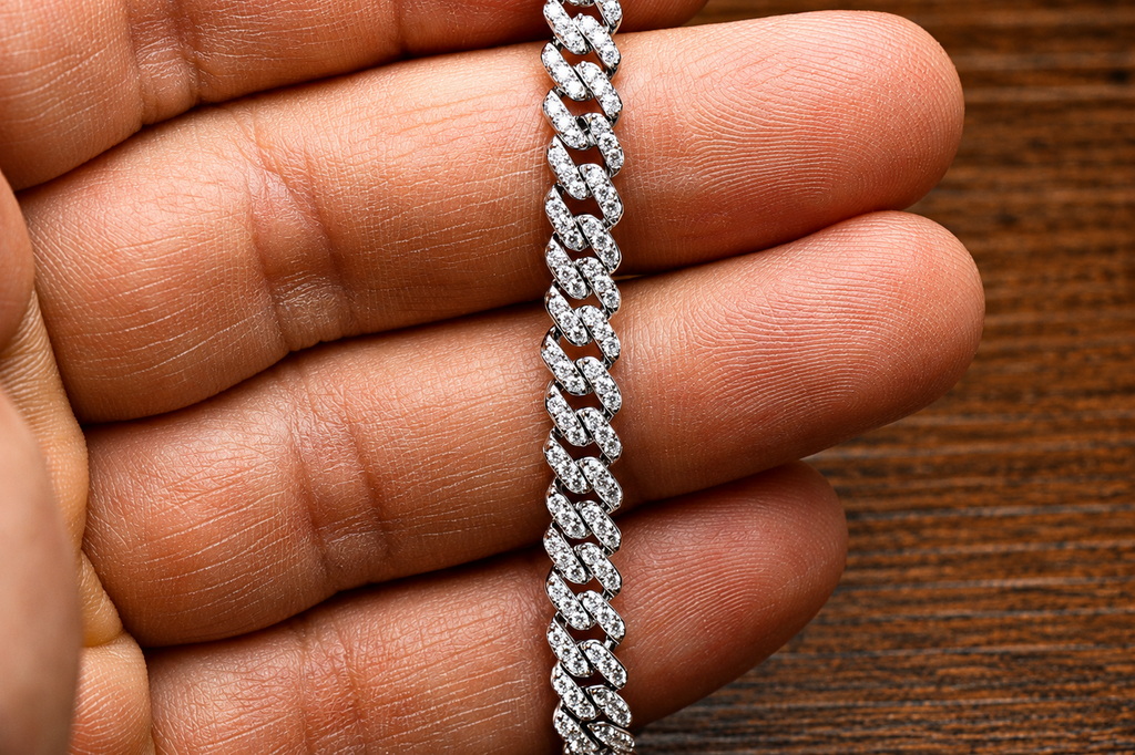 A close-up of a hand holding the VVS1 Moissanite Monaco Cuban Bracelet 5.8mm 2.01 CTW in 925 sterling silver, sparkling against a wooden surface.
