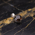 A heart-shaped brown gemstone pendant in a silver bezel setting, resting on a polished black and gold marble surface.