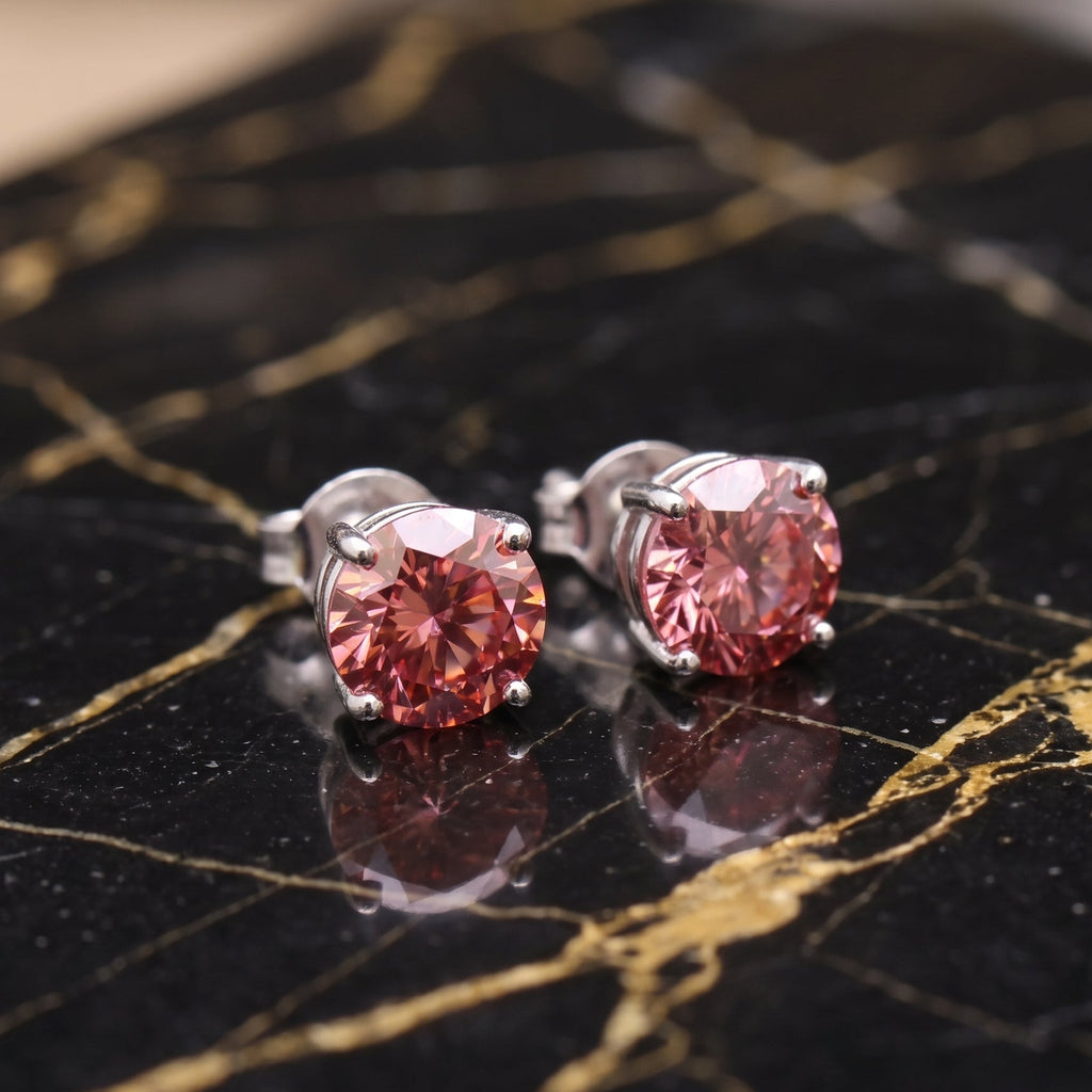 A pair of round-cut pink gemstone stud earrings in silver-toned prong settings, displayed on a black and gold veined marble surface. the most beautiful earrings you will ever see