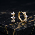 A pair of gold huggie hoop earrings adorned with clear baguette and round crystals, displayed on a black marble surface with gold veining.