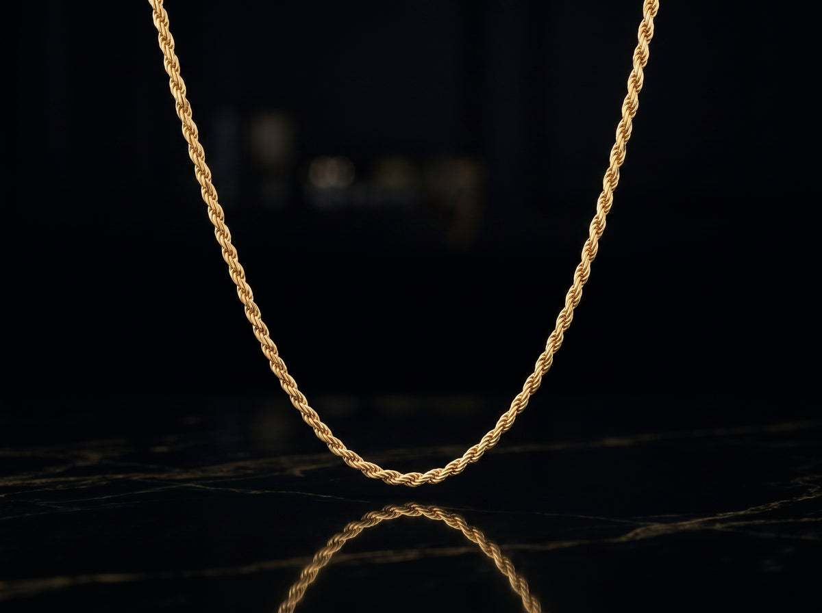 A twisted rope chain necklace in yellow gold, displayed in a U-shape against a dark, reflective black surface.