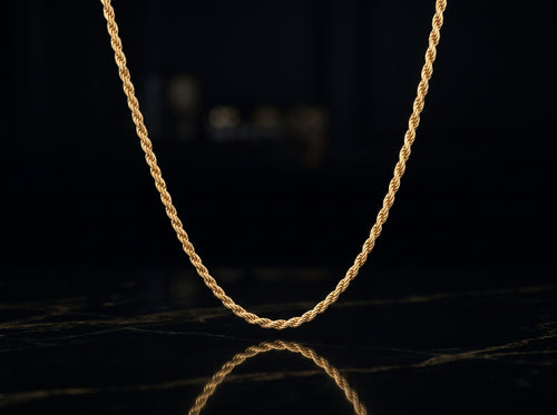 A twisted rope chain necklace in yellow gold, displayed in a U-shape against a dark, reflective black surface.