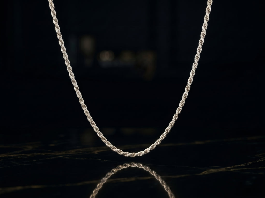 A silver twisted rope chain necklace draped in a U-shape against a dark, reflective black background.