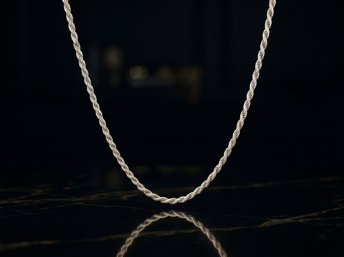 A silver twisted rope chain necklace draped in a U-shape against a dark, reflective black background.