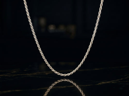 A silver twisted rope chain necklace draped in a U-shape against a dark, reflective black background.