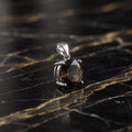 A silver pendant with a faceted brown gemstone, resting on a black and gold veined marble surface. Smokey Quartz