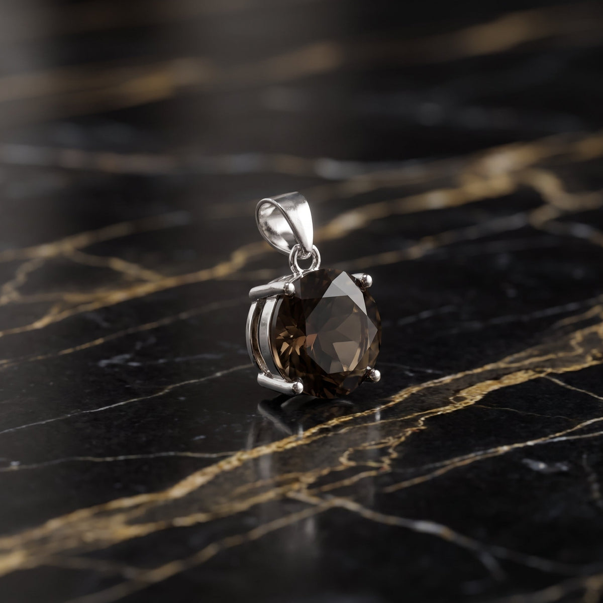 A silver pendant with a faceted brown gemstone, resting on a black and gold veined marble surface. Smokey Quartz