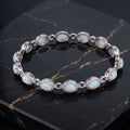 A silver-toned link bracelet featuring oval opal stones and small clear accent stones, displayed on a black marble surface.
