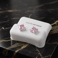 A pair of pink gemstone stud earrings in silver settings, displayed on a white silicone stand labeled 'STERLING SILVER' on a black marble surface.