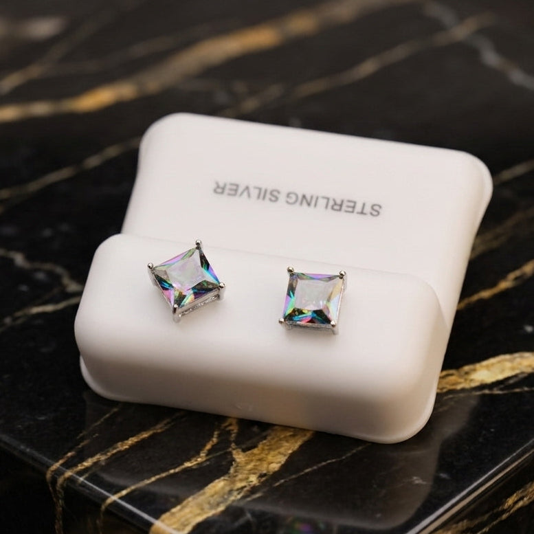 A pair of Mystic Topaz Cz Square Princess Cut 925 Sterling Silver earrings in a white case, displayed on a glossy black and gold marble surface.