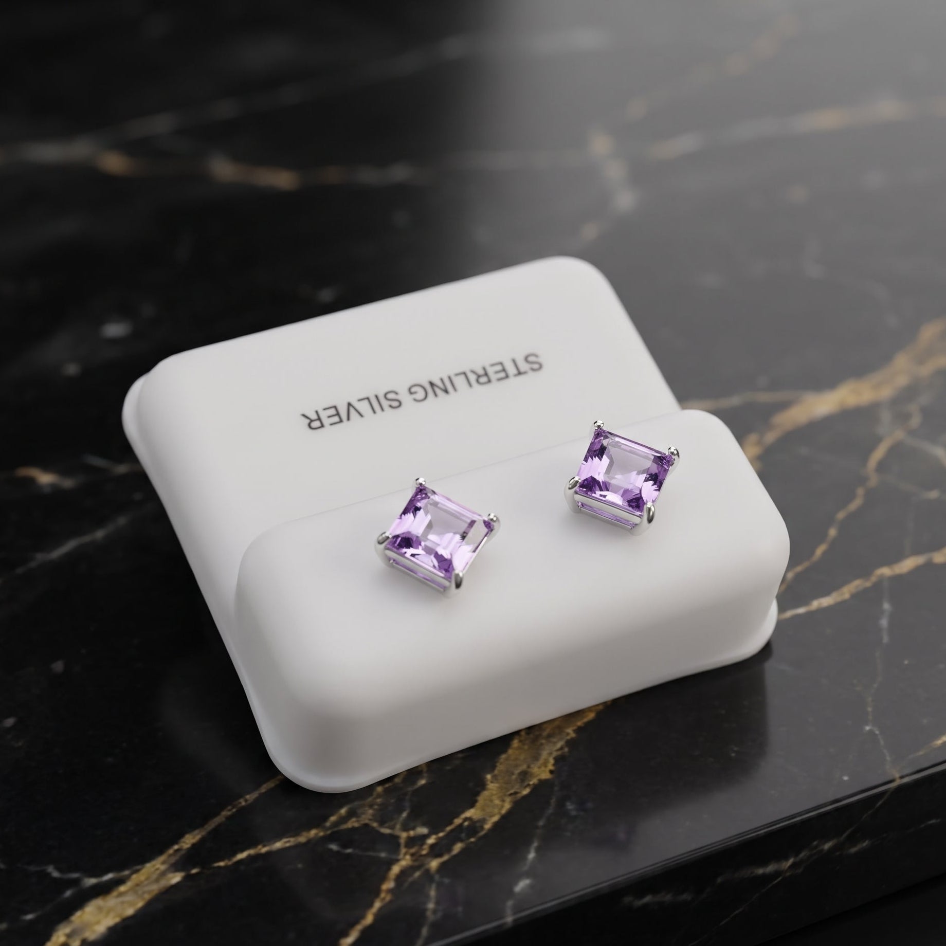 A pair of square-cut purple gemstone stud earrings in silver settings, displayed on a white jewelry stand with the text 'STERLING SILVER' on a black marble surface with gold veining.