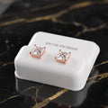 A pair of princess-cut clear cubic zirconia stud earrings in rose gold settings, displayed on a white 'STERLING SILVER' branded stand on a black marble surface with gold veining.