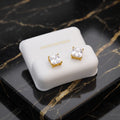 A pair of gold stud earrings with clear square-cut stones, displayed on a white jewelry box set on a black marble surface.