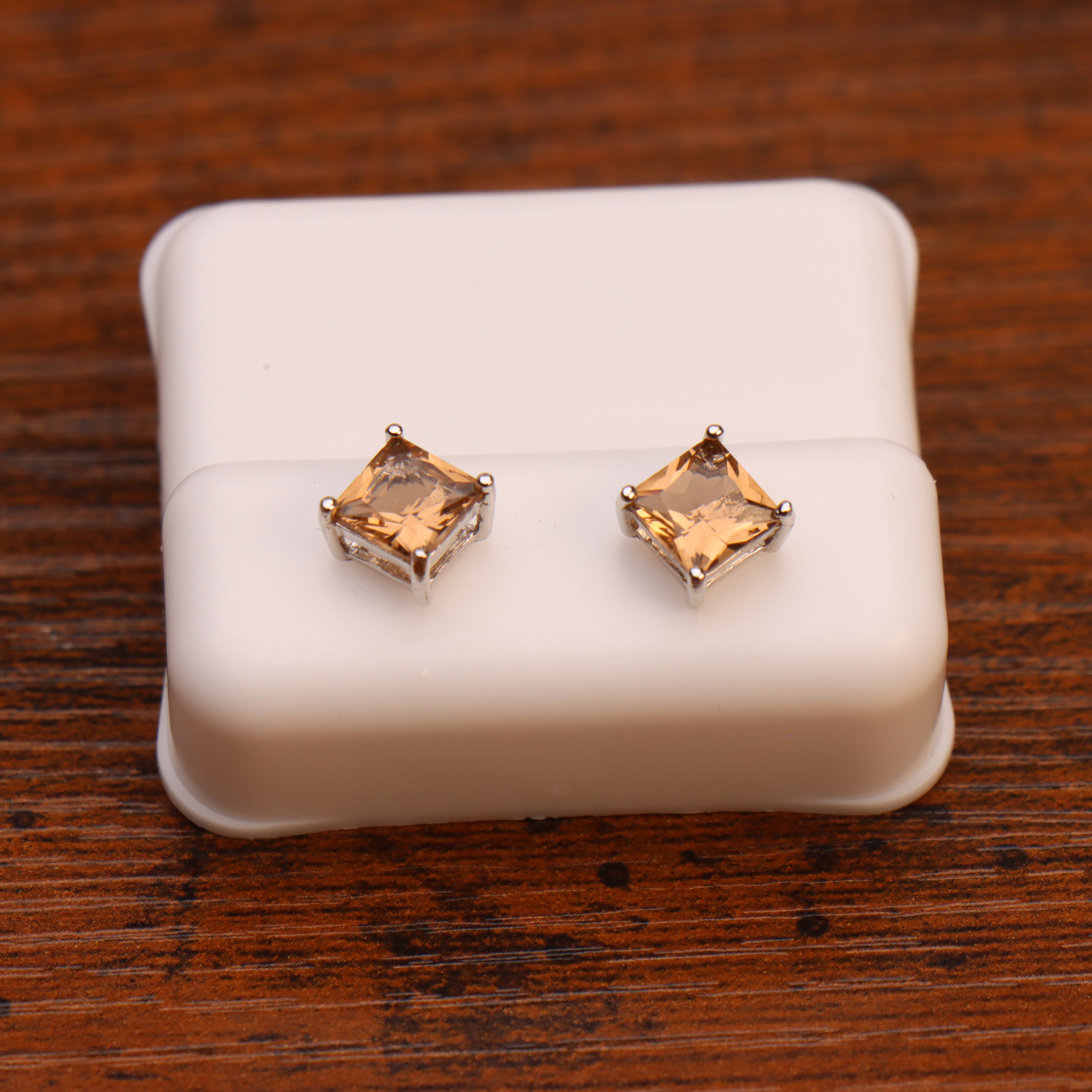 A pair of Morganite CZ square princess cut earrings in 925 sterling silver, displayed on a white jewelry holder atop a wooden surface.