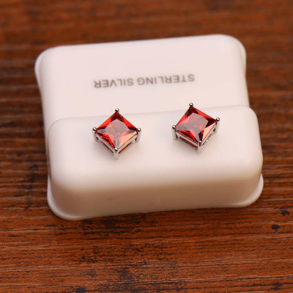 Ruby Red CZ square princess cut earrings in 925 sterling silver, displayed on a white STERLING SILVER box atop a wooden surface.