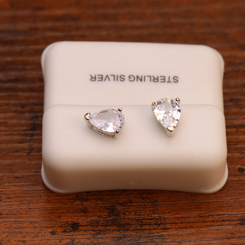 A pair of Pear Cz Earrings Clear 925 Sterling Silver 6x9mm with push backs, displayed on a white case labeled STERLING SILVER and resting on a wooden surface.