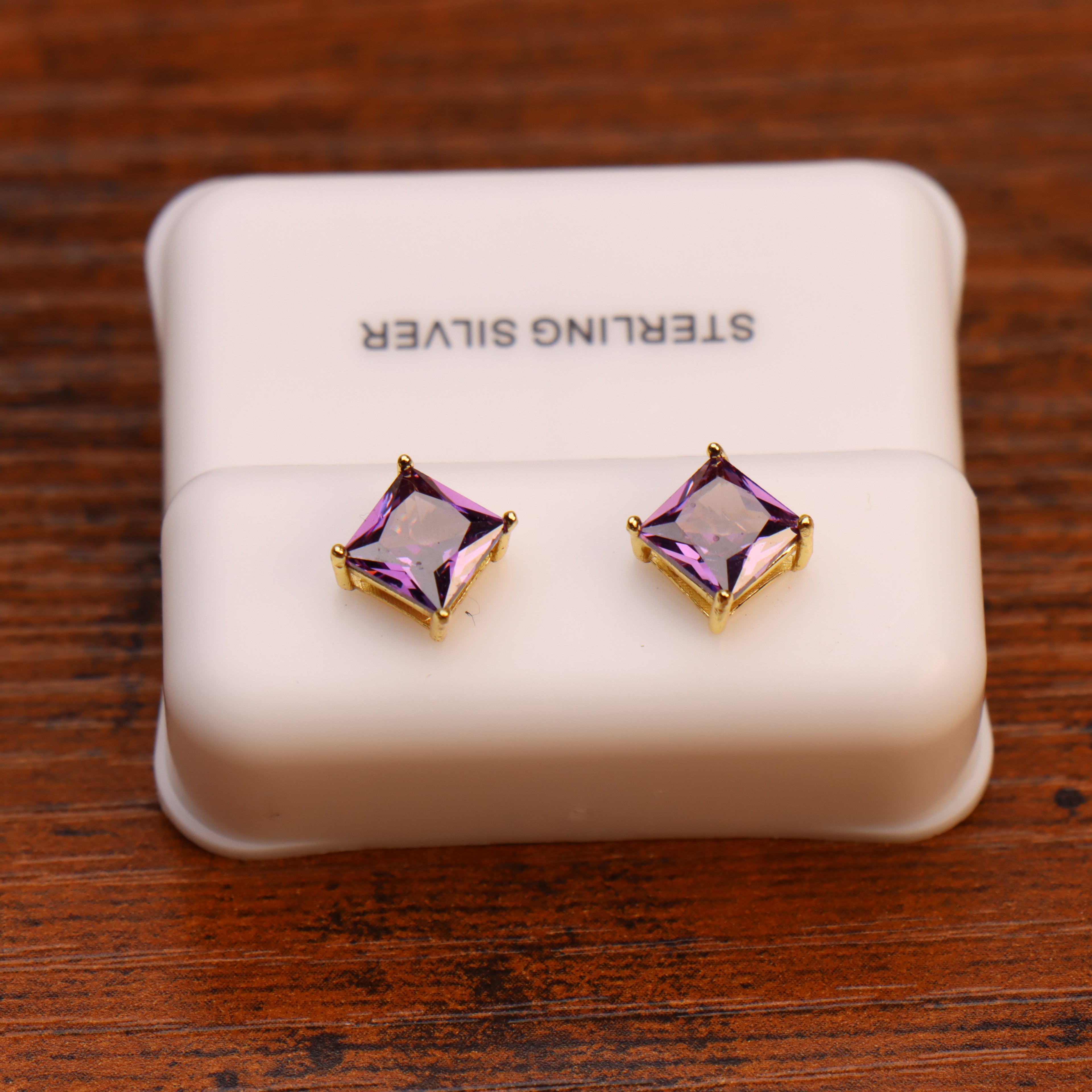 Purple square CZ stud earrings in 14k gold over 925 sterling silver on a white display stand