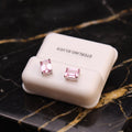 A pair of Emerald Cut Cz Earrings with 7x5mm pink sapphire stones in 925 silver, presented in a white box and displayed on black marble with beige veins.