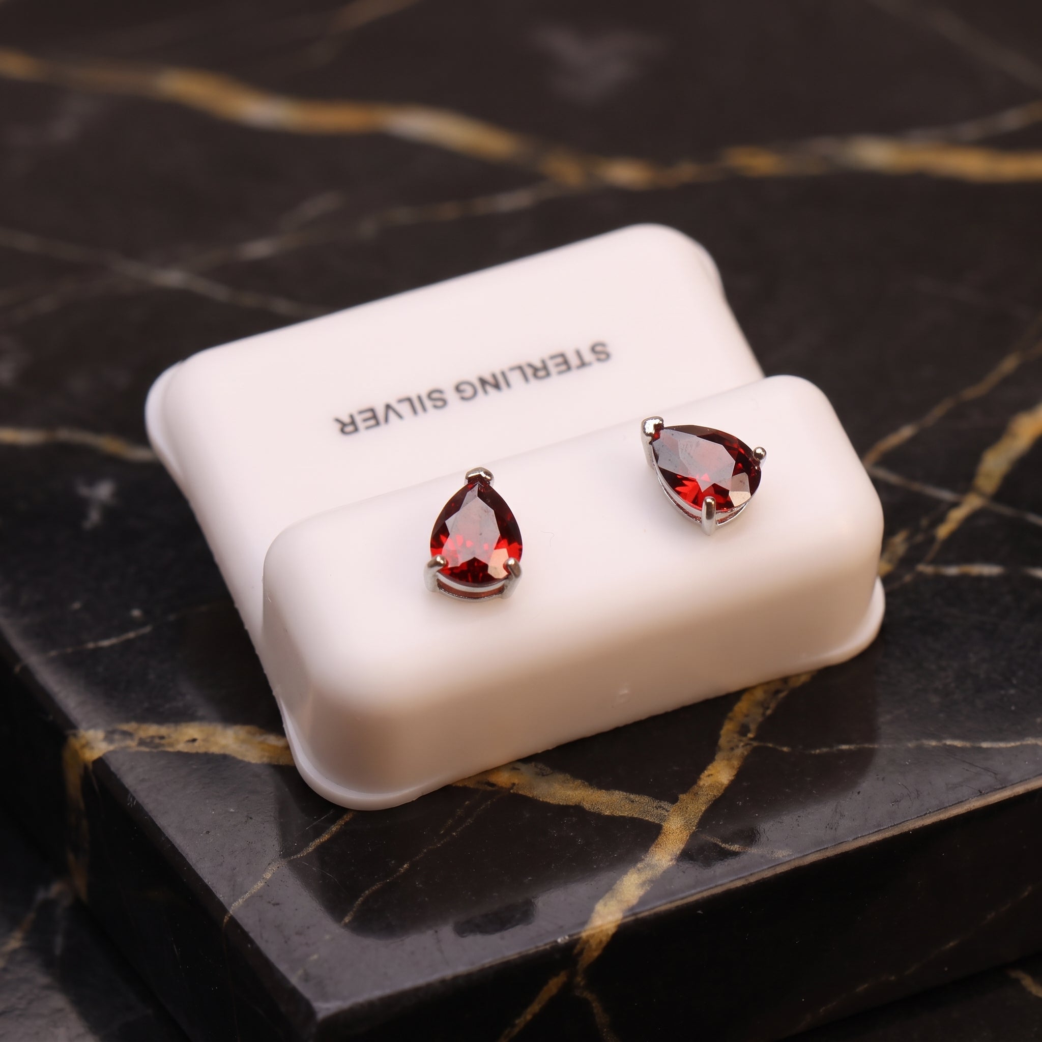 Pear shaped garnet CZ earrings in 925 sterling silver with push backs on a white display stand