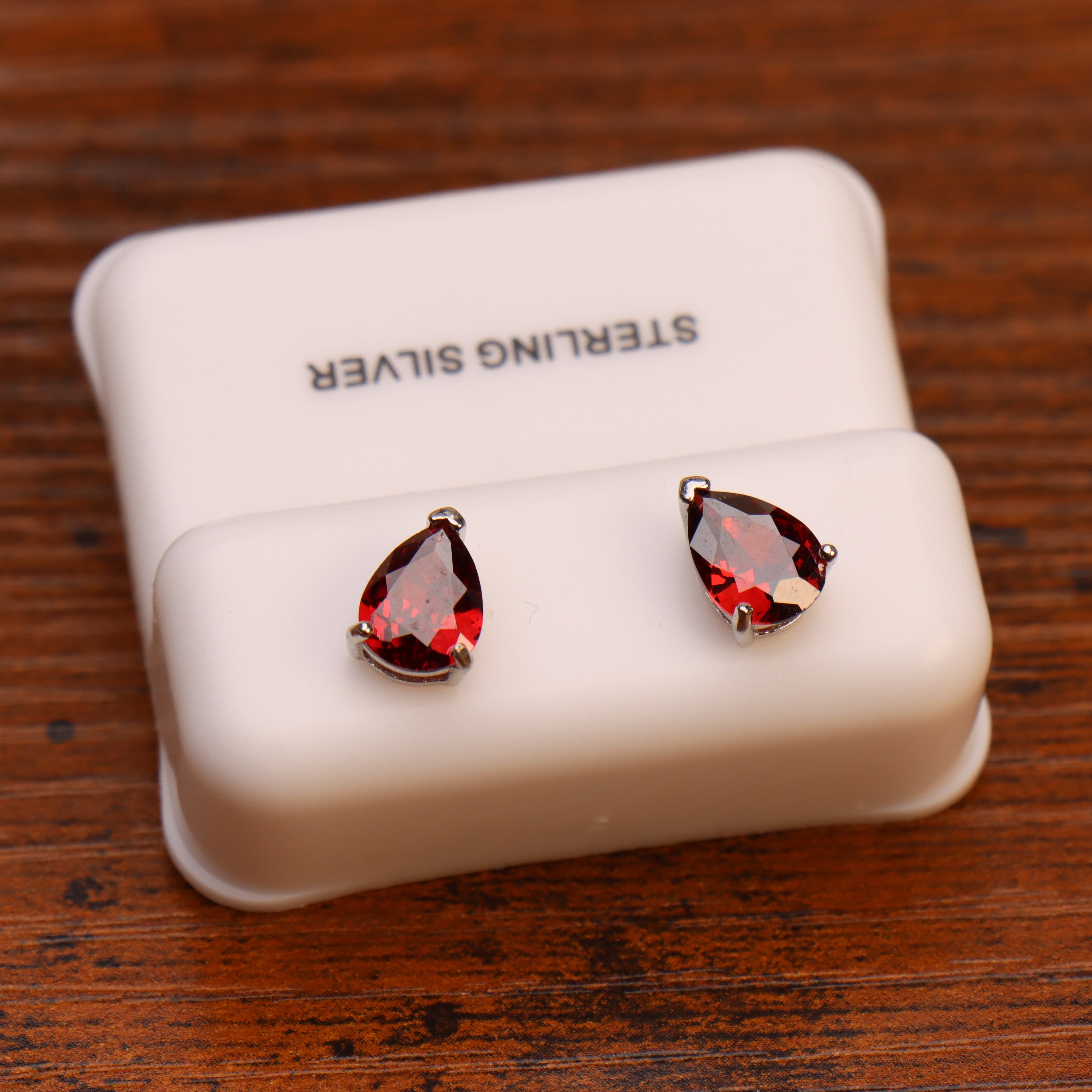 Pear shaped garnet sterling silver stud earrings on a white display stand