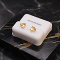 A pair of gold heart-shaped stud earrings with clear gemstones, displayed on a white 'STERLING SILVER' box placed on a black marble surface.