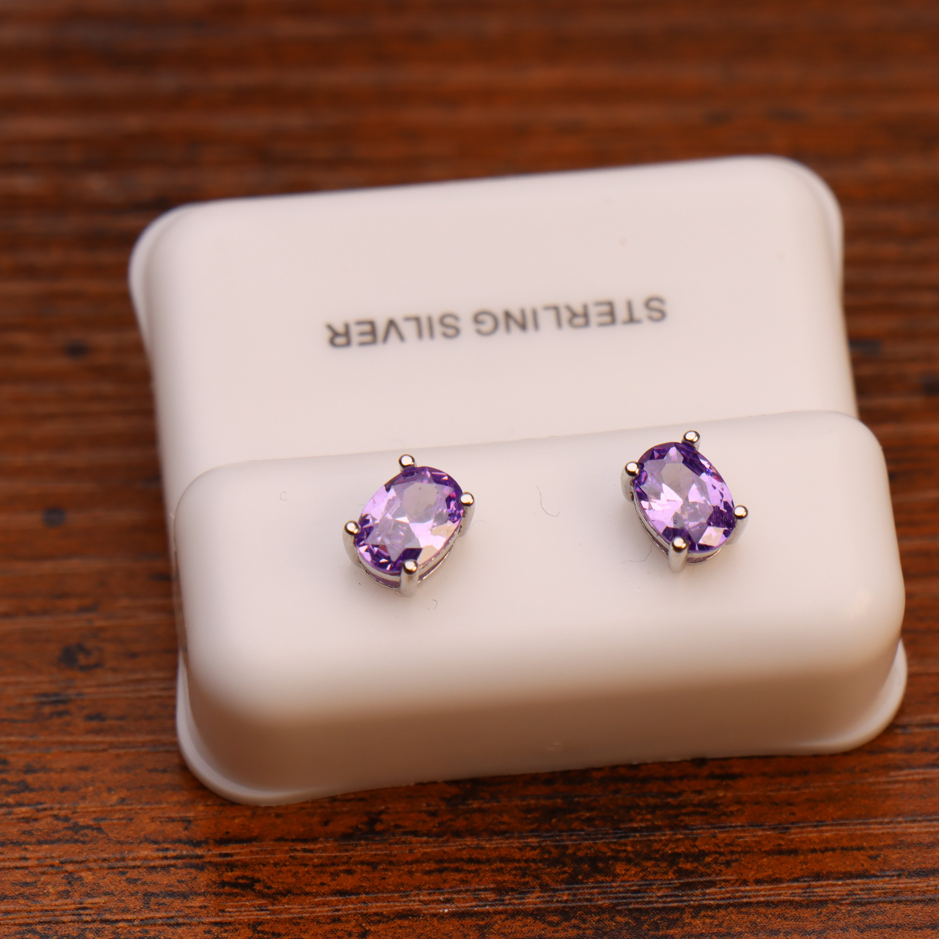 Purple oval cubic zirconia stud earrings in 925 sterling silver on a white display stand