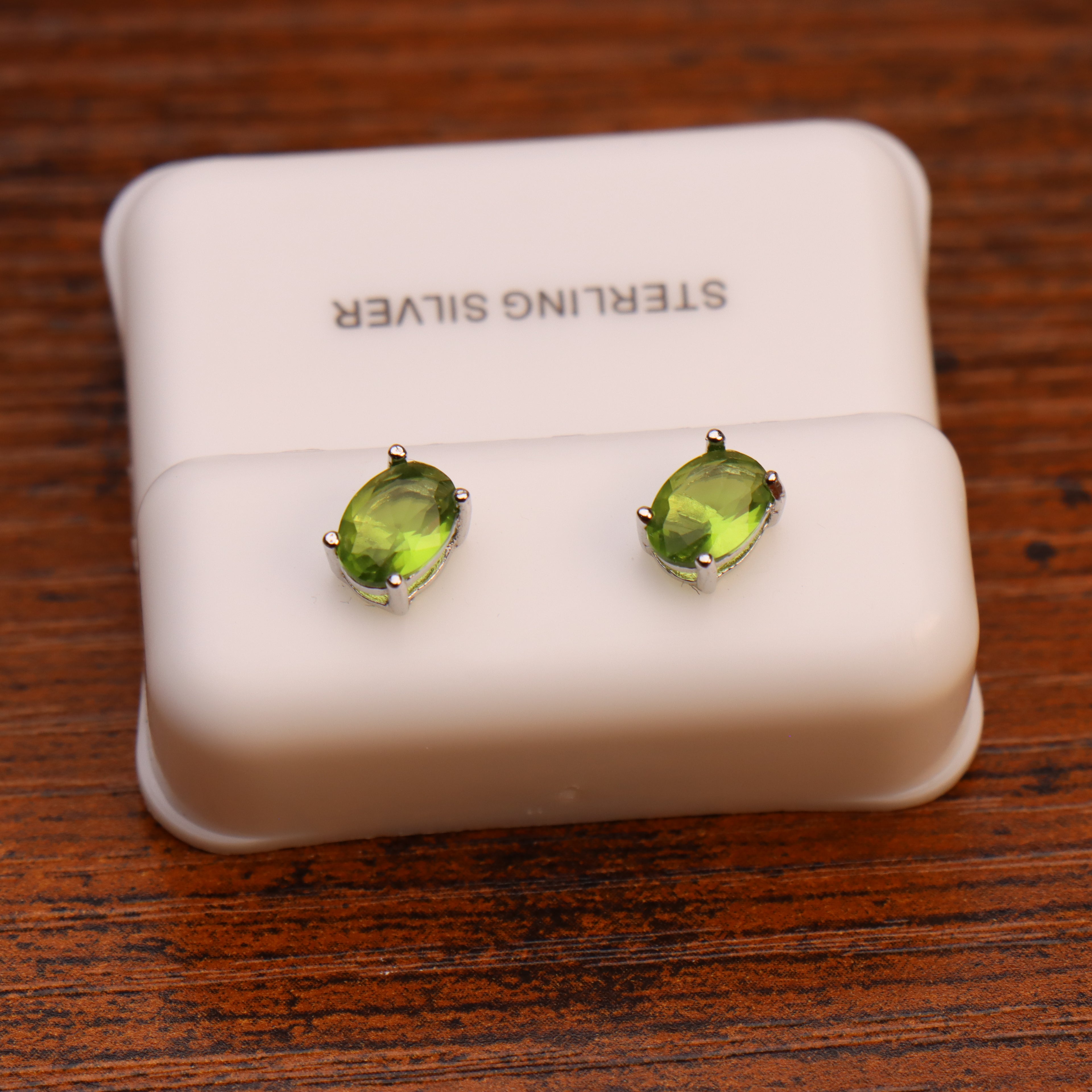 Oval peridot CZ earrings in 925 sterling silver settings on a white display stand