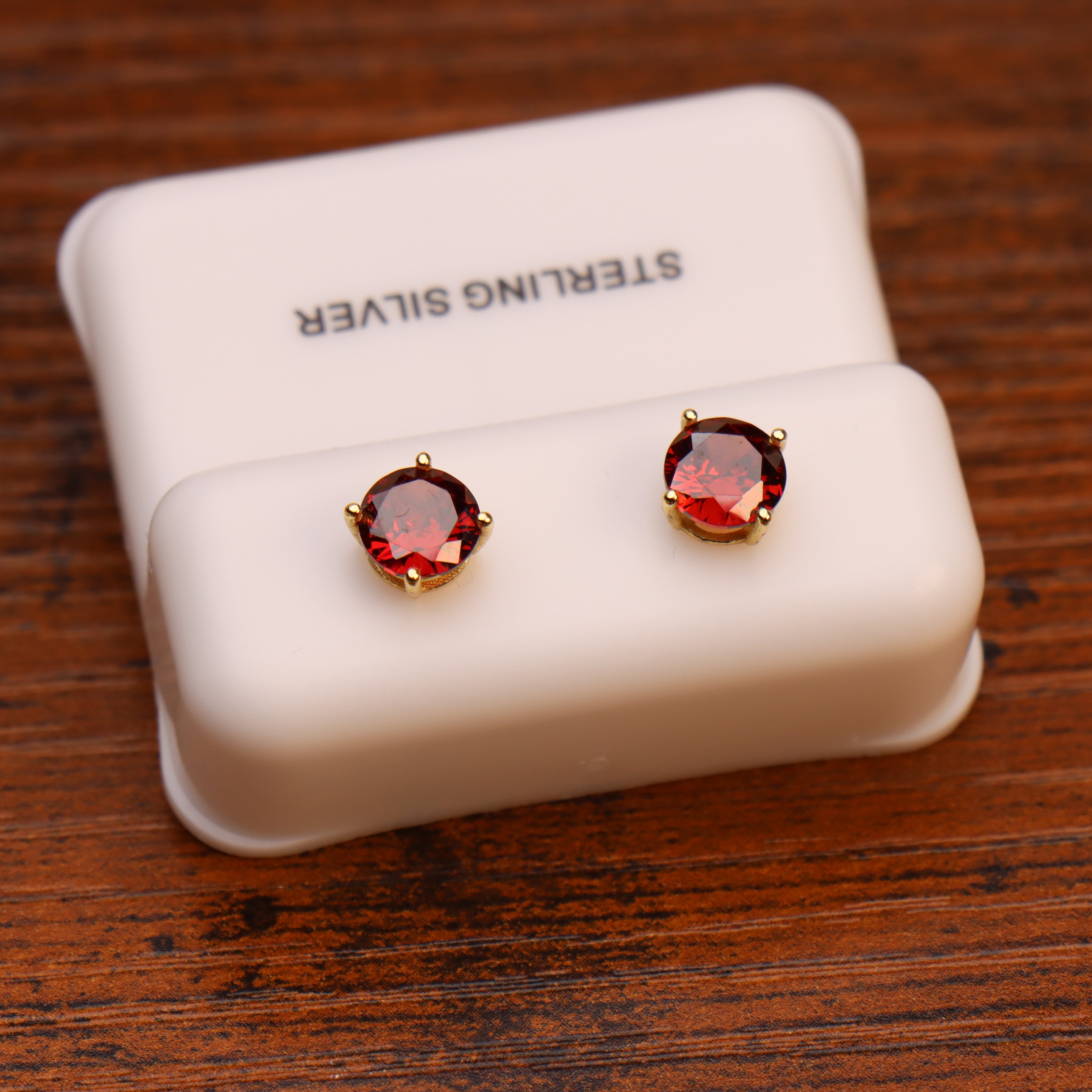 Ruby red round 6mm CZ stud earrings in 14k gold over 925 sterling silver on a white display stand