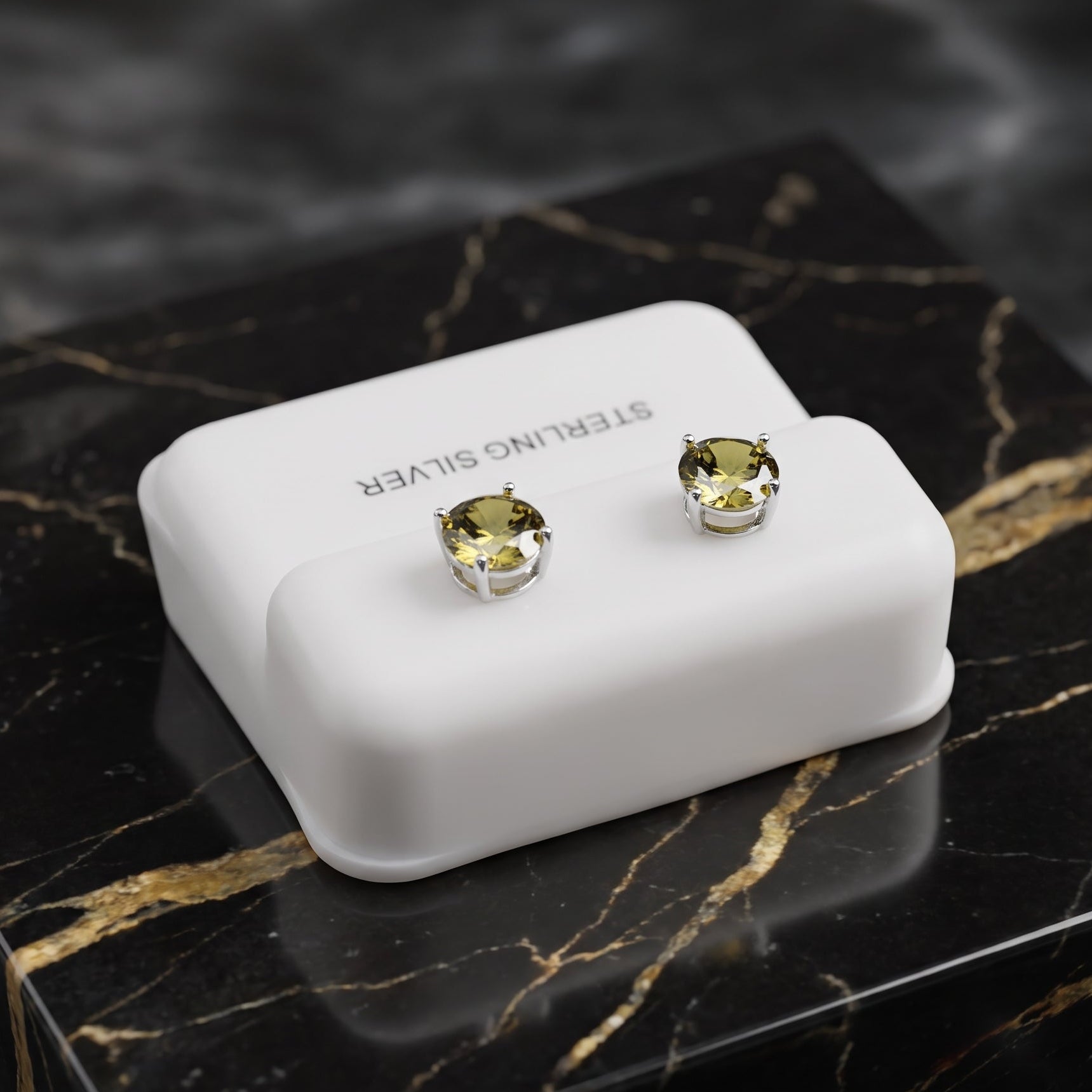 Sterling silver stud earrings with round yellow-green gemstones, displayed on a white rectangular jewelry stand placed on a black marble box.