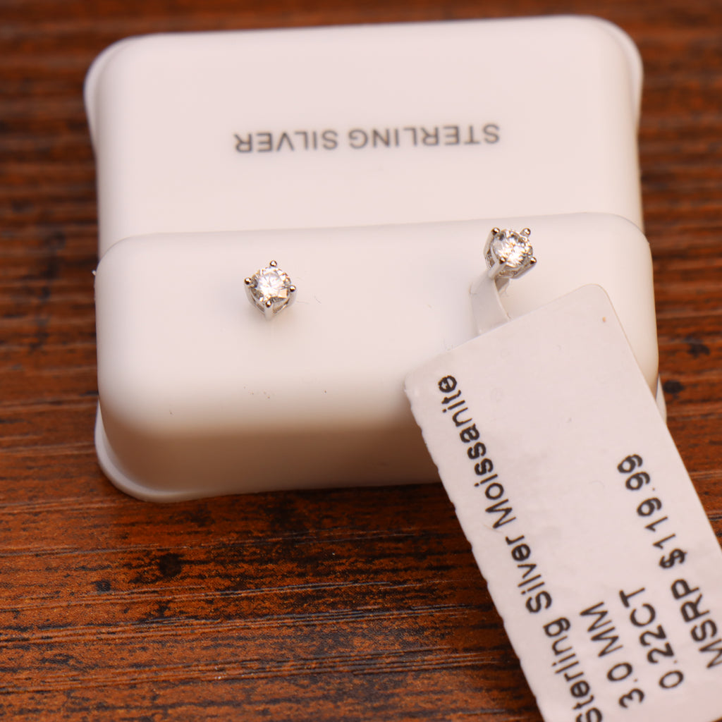 A pair of small silver stud earrings with clear gemstones displayed on a white jewelry box, with a price tag attached and the words 'STERLING SILVER' visible on the box and tag.