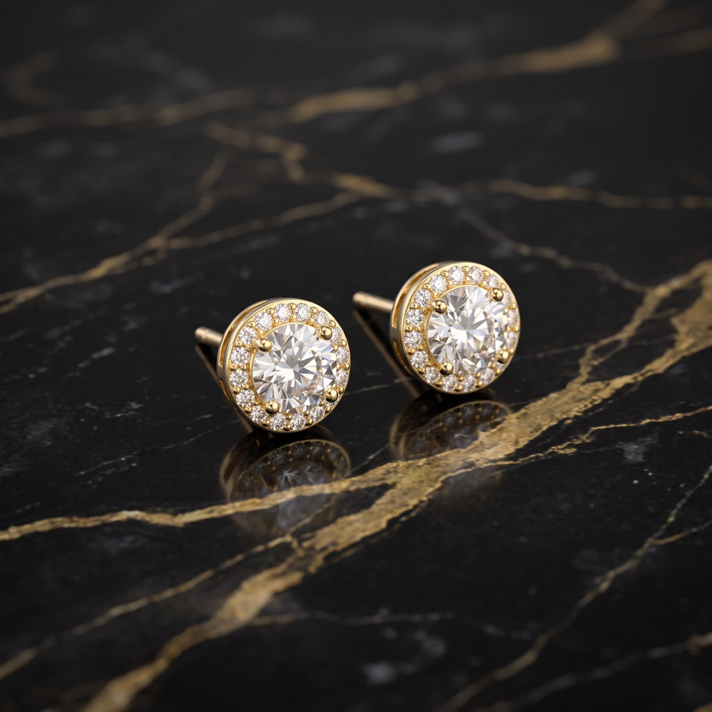 A pair of round gold stud earrings with halo settings, each featuring a central clear gemstone surrounded by smaller clear stones, displayed on a black marble surface with gold veining.