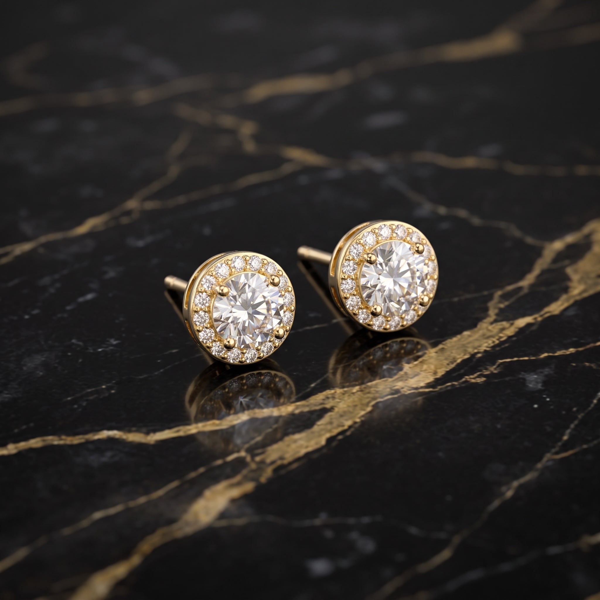 A pair of round gold stud earrings with halo settings, each featuring a central clear gemstone surrounded by smaller clear stones, displayed on a black marble surface with gold veining.