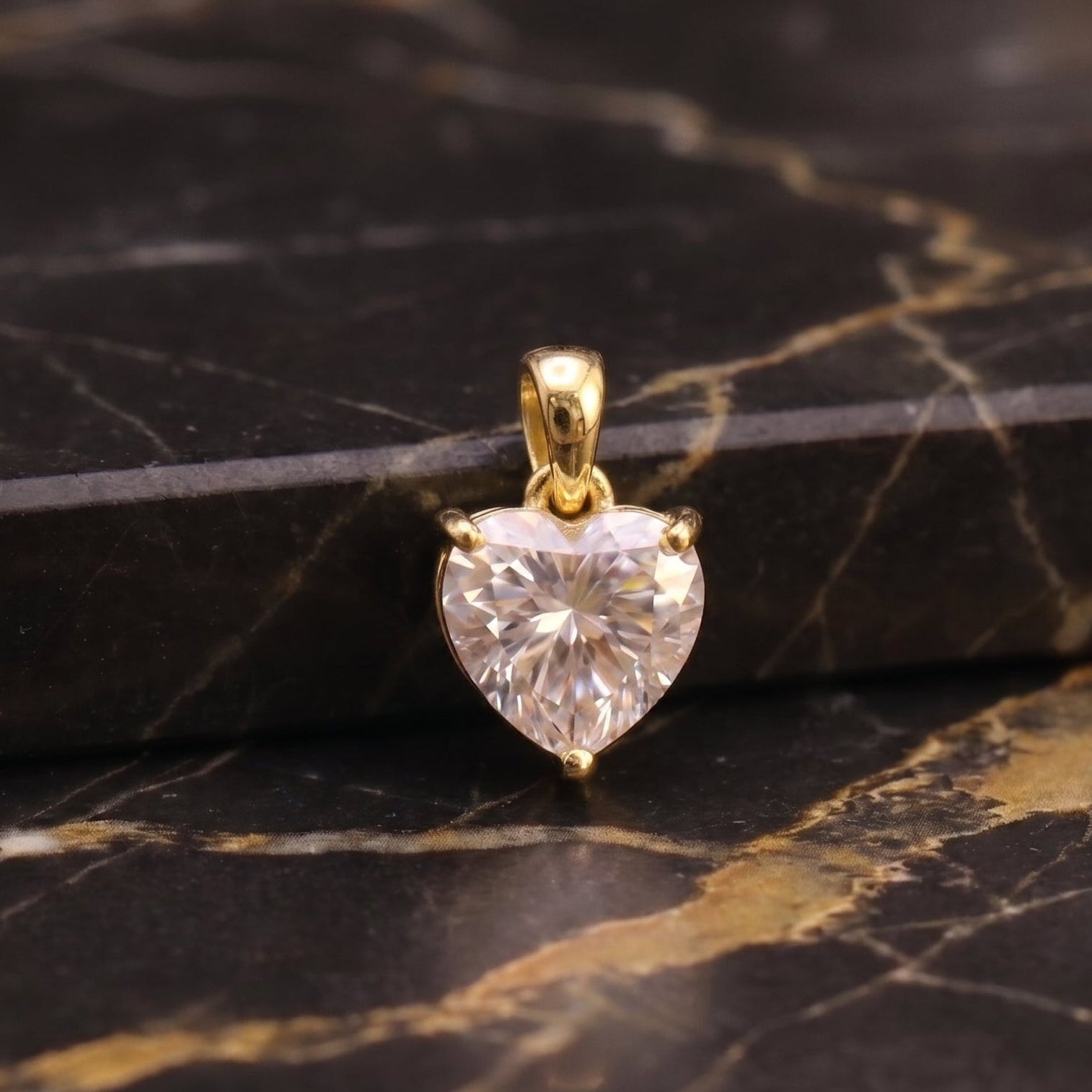 A heart-shaped clear gemstone pendant in a gold setting, displayed on a black and gold marble surface.