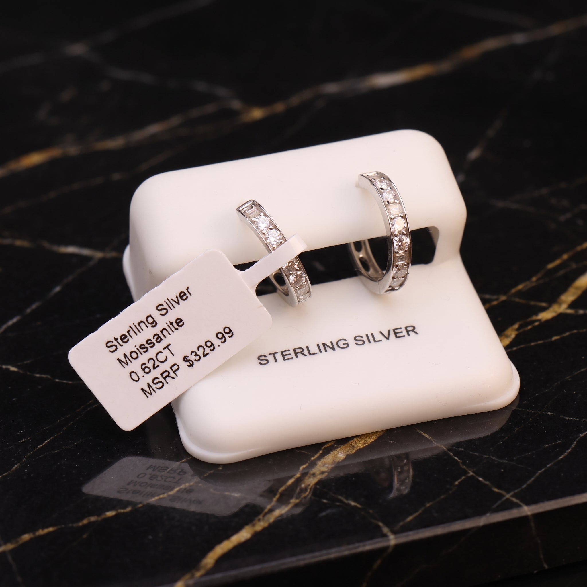 A pair of sterling silver rings displayed on a white jewelry stand, with a paper tag reading 'Sterling Silver Moissanite 0.62CT MSRP $329.
