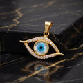 Gold evil eye pendant with a blue and black glass eye center and clear crystal accents, displayed on a black marble surface next to a black box.