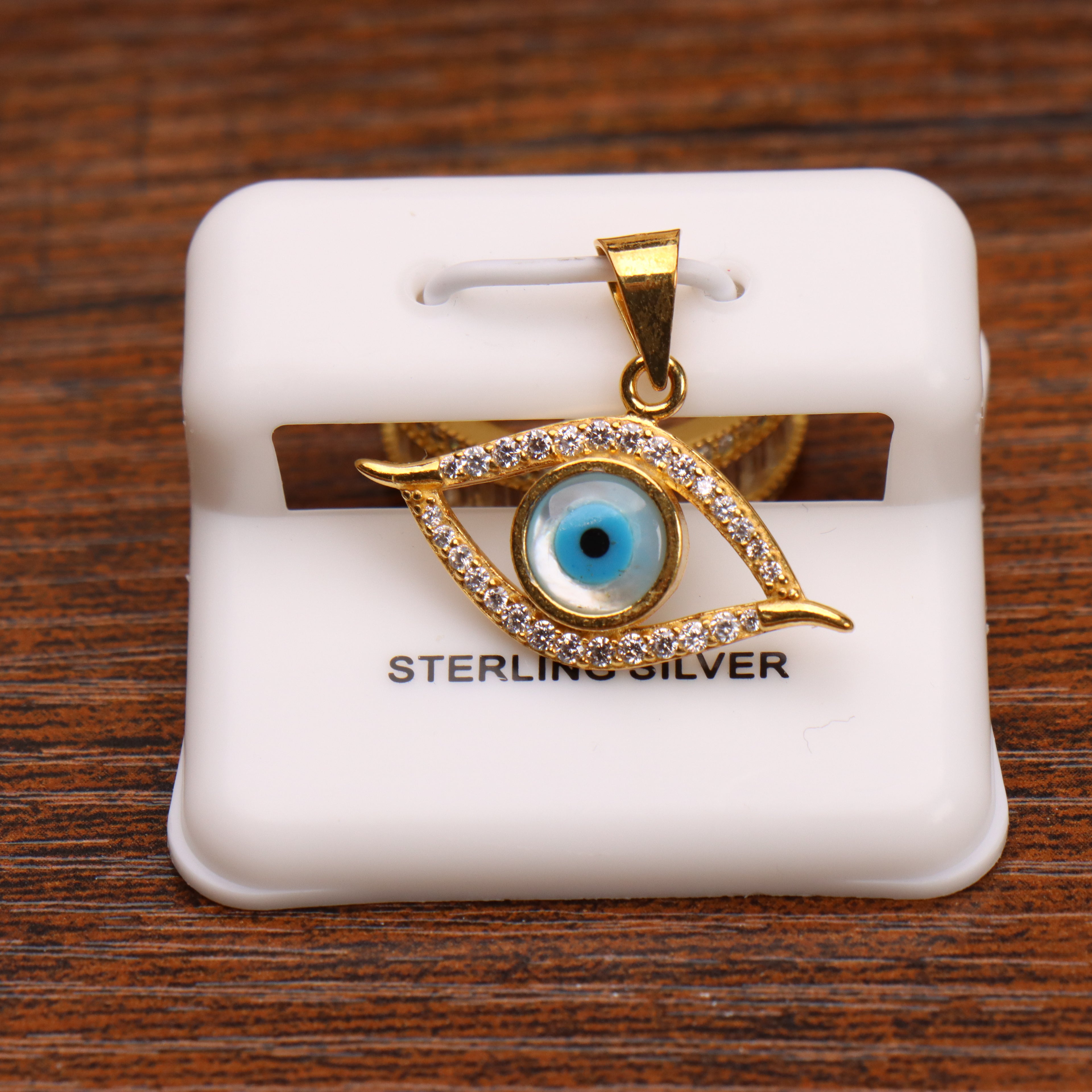 Evil eye pendant charm in 14k gold over sterling silver with clear stones on a white display stand