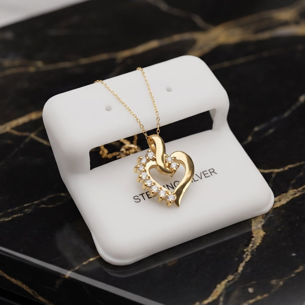 A gold heart pendant necklace with a pavé-set heart on a white display card, placed on a black marble tray.