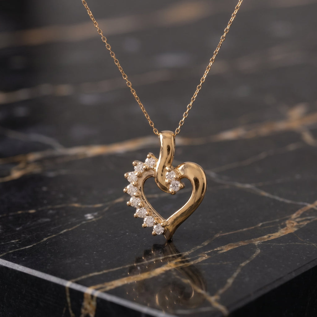 A gold heart-shaped pendant necklace with a row of small clear stones along one side, displayed on a black marble surface.
