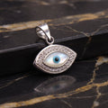 A sterling silver evil eye pendant with a white mother-of-pearl background and a blue iris, displayed on a black and gold marble surface.