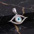 A sterling silver evil eye pendant with a blue and white glass eye in the center, surrounded by small clear crystals, resting on a black marble surface with gold veining.