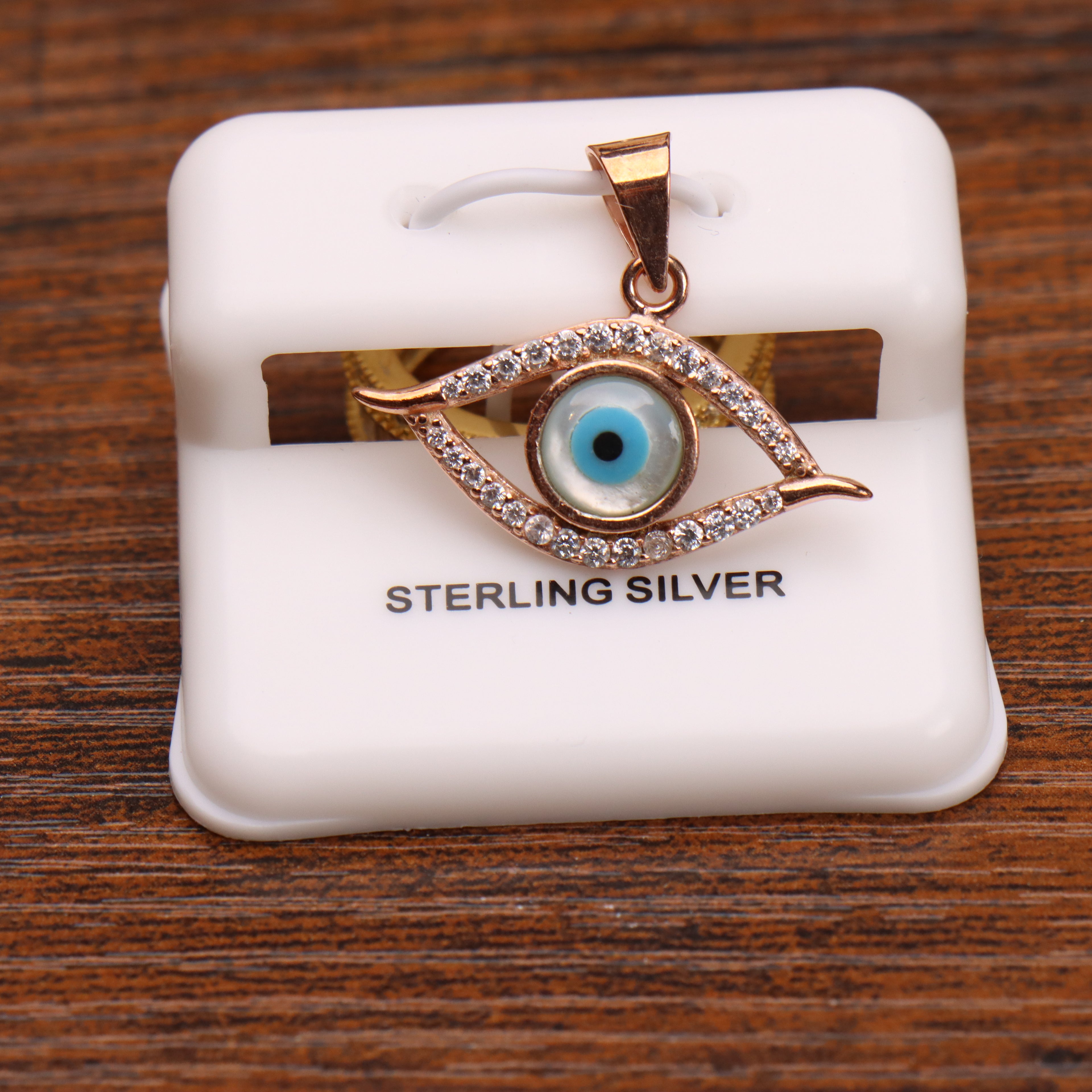Rose gold sterling silver evil eye pendant charm with crystals on a white display stand