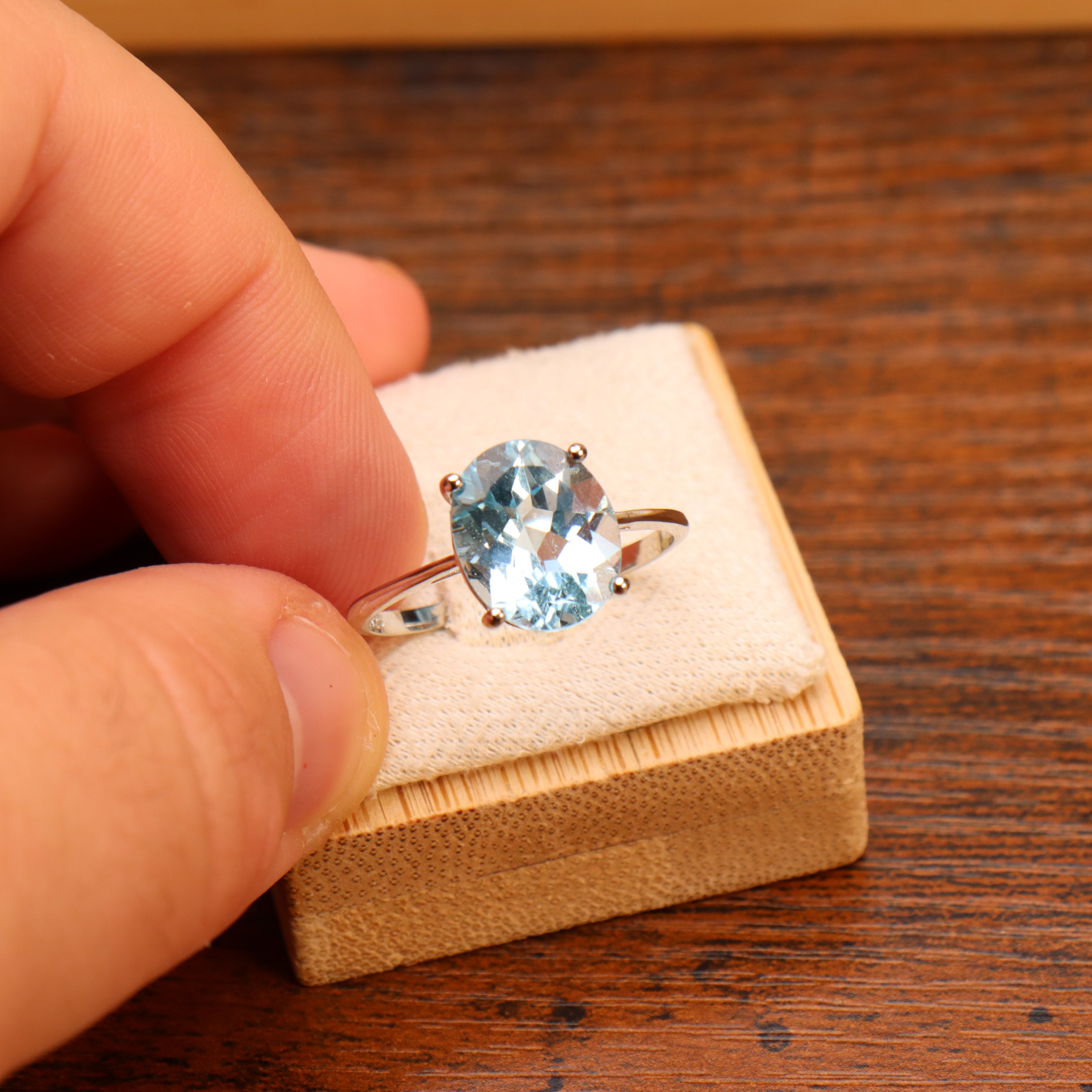 Oval cut blue topaz ring in 925 sterling silver held over a wooden jewelry box