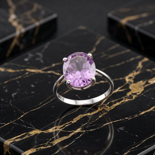 A silver ring with a large oval light purple amethyst gemstone, displayed on a black and gold marble surface.