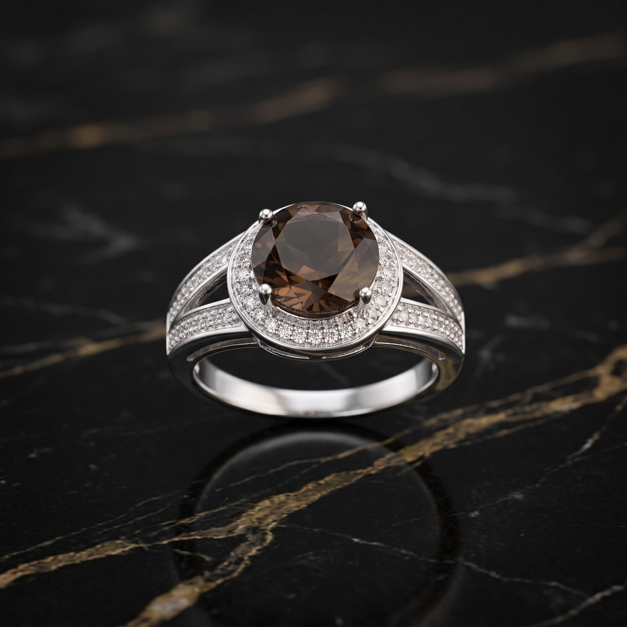 A silver-toned ring featuring a large oval brown smoky gemstone in a prong setting, surrounded by a double halo of small clear pavé stones, displayed on a black marble surface with gold veining.