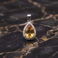 Citrine pear pendant with halo of CZ stones in 925 sterling silver on black marble surface