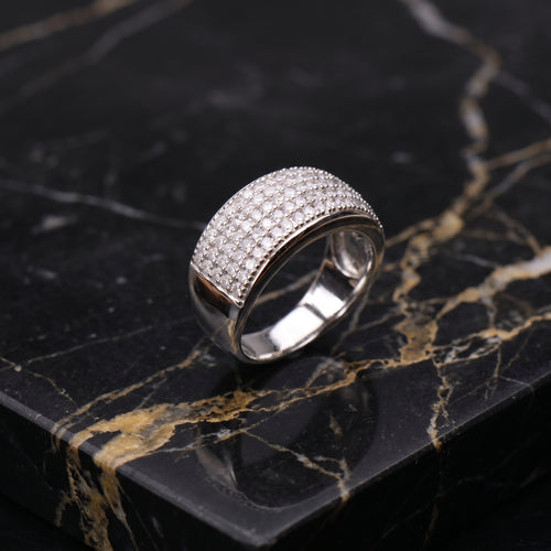 A silver pavé ring with a curved, multi-row setting of small clear stones, displayed on a black marble surface with gold veining.